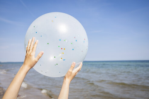 Hände eines Mädchens, das einen Luftballon am Strand hält - OJF00285