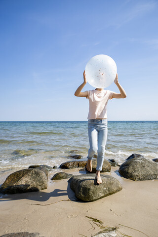Mädchen steht auf Steinen am Strand und hält einen Luftballon, lizenzfreies Stockfoto