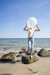 Girl standing on stones at the beach holding a balloon - OJF00287