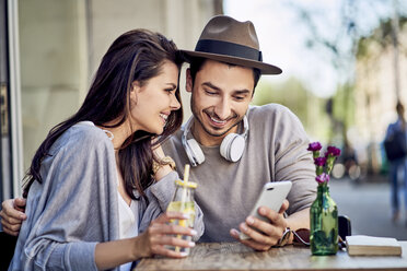 Happy young couple looking at cell phone at outdoors cafe - BSZF00787