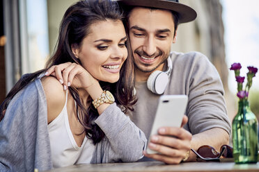 Happy young couple using cell phone at outdoors cafe - BSZF00788