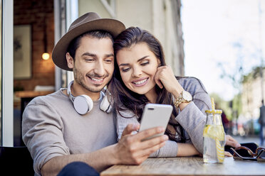 Glückliches junges Paar schaut in einem Café im Freien auf sein Handy - BSZF00794