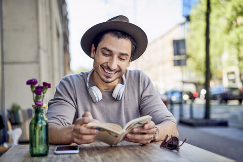 Glücklicher junger Mann, der in einem Café im Freien ein Buch liest, lizenzfreies Stockfoto