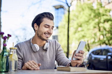 Happy young man using cell phone at outdoors cafe - BSZF00799