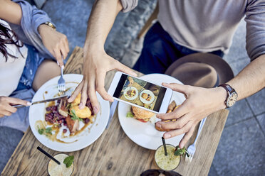 Overhead view of couple taking photo of food at outdoors restaurant - BSZF00800