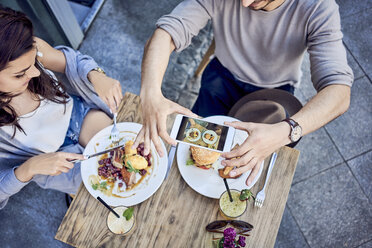 Draufsicht auf ein Paar, das sein Essen in einem Restaurant im Freien fotografiert - BSZF00801