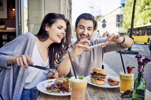 Glückliches junges Paar beim Fotografieren von Essen im Restaurant im Freien - BSZF00802