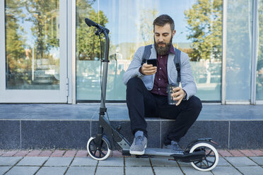 Geschäftsmann sitzt im Freien und benutzt ein Mobiltelefon neben einem Motorroller - ZEDF01704