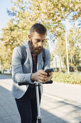 Businessman checking cell phone on scooter - ZEDF01708