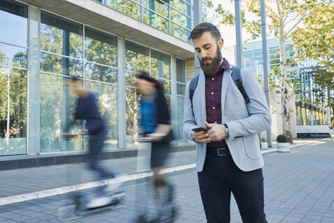 Businessman using cell phone with commuters riding on scooters stock photo