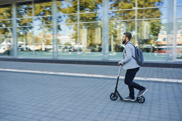 Businessman riding scooter along office building - ZEDF01711