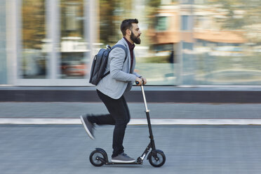 Businessman riding scooter along office building - ZEDF01713