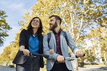 Happy businessman and businesswoman with scooters - ZEDF01717