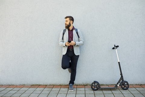 Businessman with scooter and cell phone leaning against a wall stock photo