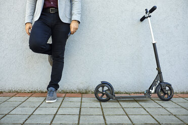 Niedriger Ausschnitt eines Geschäftsmannes mit Motorroller und Handy, der an einer Wand lehnt - ZEDF01721