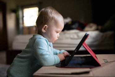 Baby-Mädchen, das einen Tablet-Computer benutzt, während es zu Hause neben einer Box steht - CAVF51477