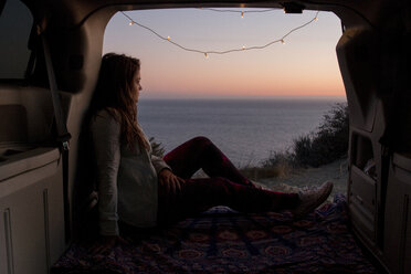 Thoughtful woman looking at view while sitting in pick-up truck against sea during sunset - CAVF51484