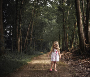 Girl standing on dirt road amidst forest - CAVF51504