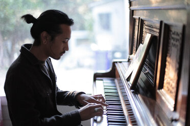 Man playing piano against window at home - CAVF51507