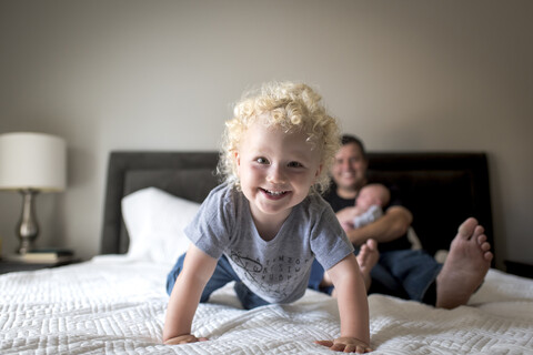 Porträt eines fröhlichen Jungen mit Vater, der seinen Bruder zu Hause auf dem Bett trägt, lizenzfreies Stockfoto