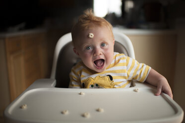Portrait of cute baby boy playing with breakfast cereal while sitting on high chair - CAVF51559