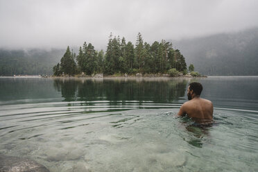 Rückansicht eines Mannes ohne Hemd, der in einem See im Wald schwimmt - CAVF51565