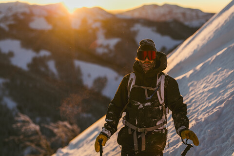 Mann in Skikleidung auf einem schneebedeckten Berg bei Sonnenuntergang, lizenzfreies Stockfoto