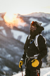 Man with skies standing on snow covered mountain against sky during sunset - CAVF51582