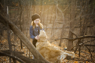 Girl petting dog while standing amidst trees at park - CAVF51588