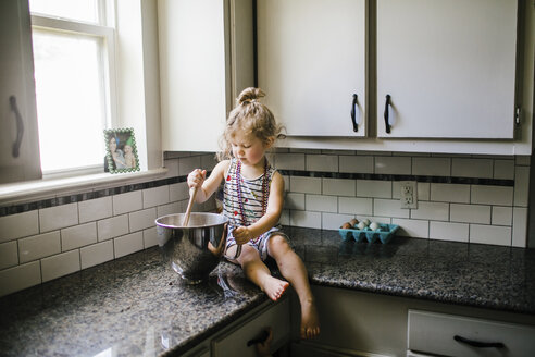 Mädchen bereitet Essen in einem Behälter zu, während sie zu Hause auf der Küchentheke sitzt - CAVF51590