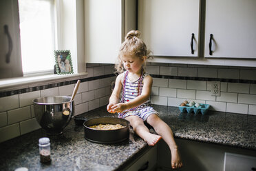 Girl preparing food in container while sitting on kitchen counter - CAVF51592