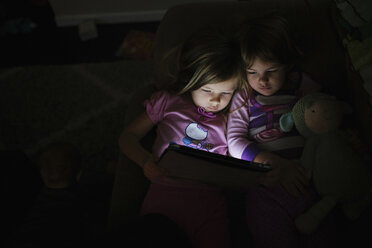 Blick von oben auf die Schwestern, die einen Tablet-Computer halten, während sie auf dem Sofa in der Dunkelkammer zu Hause liegen - CAVF51617
