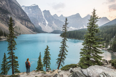 Hoher Blickwinkel auf eine Frau, die auf einem Felsen am See im Banff National Park steht - CAVF51654