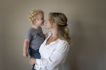 Cheerful mother carrying son against wall at home - CAVF51663