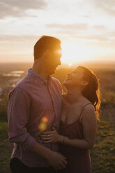Fröhliches junges Paar steht bei Sonnenuntergang auf einem Feld - CAVF51664