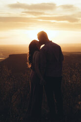 Junges Paar, das sich küsst, während es auf einem Feld gegen den Himmel bei Sonnenuntergang steht - CAVF51666