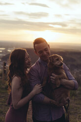 Junges Paar mit Hund bei Sonnenuntergang auf einem Feld stehend - CAVF51667
