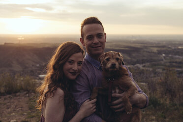 Portrait of young couple with dog standing on field during sunset - CAVF51668