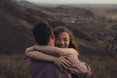 Loving young couple embracing on field against mountains - CAVF51671