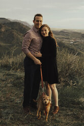 Ganzkörperporträt eines jungen Paares mit Hund auf einem Feld bei Sonnenuntergang - CAVF51675
