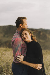Seitenansicht eines jungen Paares, das sich umarmt, während es auf einem Feld steht - CAVF51678