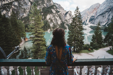 Junge Frau betrachtet die Aussicht, während sie auf dem Balkon vor Bergen und See steht - CAVF51698