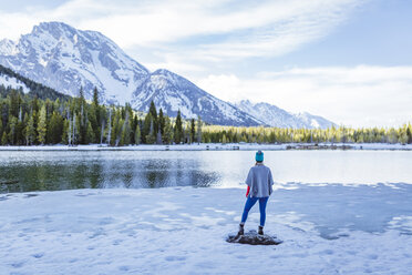 Rear view of woman standing on rock amidst frozen lake against mountains during winter - CAVF51709