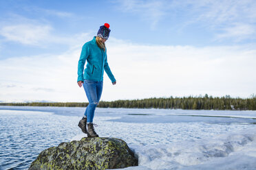 Full length of woman standing on rock amidst frozen lake against sky - CAVF51712