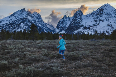 Rückansicht einer Frau, die im Winter auf einem Feld gegen Berge läuft - CAVF51716