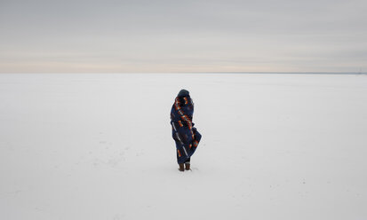 Rückansicht einer in eine Decke eingewickelten Frau, die auf einer verschneiten Landschaft vor dem Himmel steht - CAVF51719