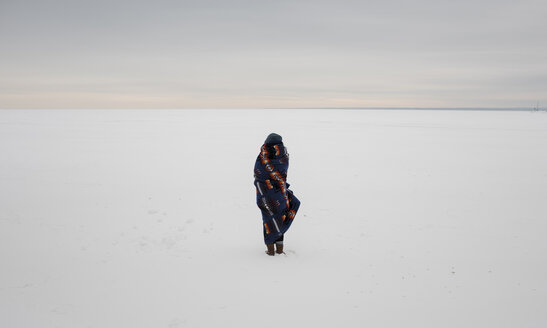 Rear view of woman wrapped in blanket standing on snow covered landscape against sky - CAVF51719