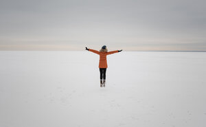 Rear view of woman with arms outstretched standing on snow covered landscape against cloudy sky - CAVF51721