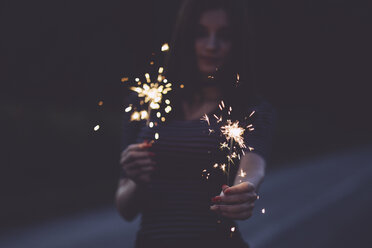 Woman holding sparklers while standing on road at night - CAVF51769