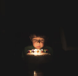 Boy blowing birthday candles on cake in darkroom - CAVF51781